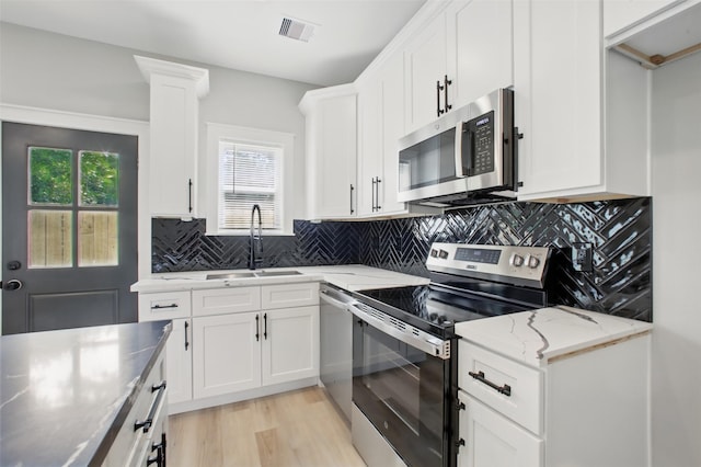 4719 Mallow St, Houston, TX 77033 - kitchen with appliances with stainless steel finishes, light wood-style flooring, white cabinetry, decorative backsplash, and light stone countertops