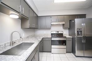 6601 Sands Point Dr Unit 59, Houston, TX 77074 - kitchen featuring appliances with stainless steel finishes, light tile patterned floors, range hood, and gray cabinets