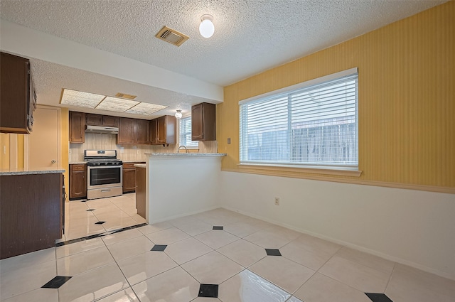 5615 Briarwood Forest Dr, Houston, TX 77088 - kitchen with stainless steel gas range oven, under cabinet range hood, a textured ceiling, light tile patterned flooring, and a peninsula