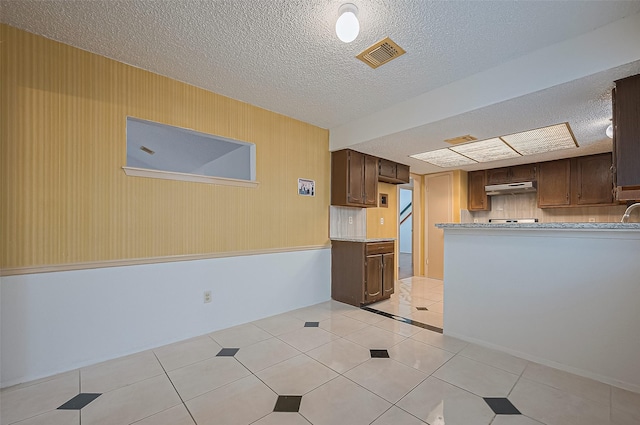 5615 Briarwood Forest Dr, Houston, TX 77088 - kitchen with under cabinet range hood, light countertops, dark brown cabinetry, a textured ceiling, and light tile patterned floors