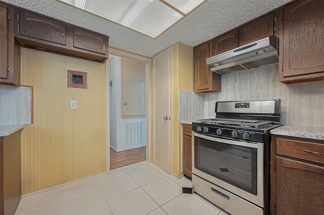 5615 Briarwood Forest Dr, Houston, TX 77088 - kitchen featuring gas range, under cabinet range hood, light tile patterned floors, and dark brown cabinets