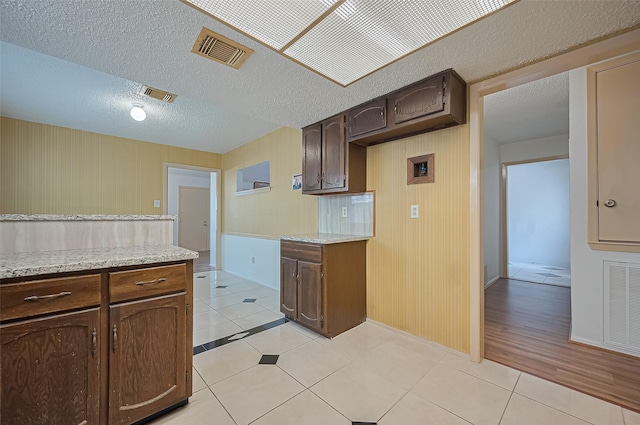 5615 Briarwood Forest Dr, Houston, TX 77088 - kitchen with light tile patterned flooring, dark brown cabinets, wood walls, light stone countertops, and a textured ceiling