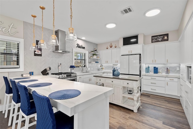 5411 Holly View Dr, Houston, TX 77091 - kitchen with open shelves, wall chimney range hood, freestanding refrigerator, a peninsula, and tasteful backsplash