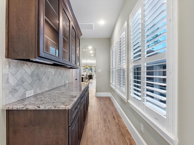 11913 Barryknoll Ln, Houston, TX 77024 - kitchen featuring dark brown cabinetry, backsplash, glass insert cabinets, light stone countertops, and light wood-style floors