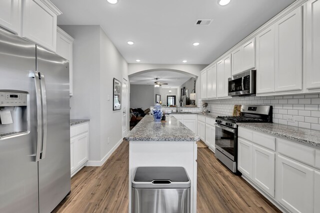 12350 Castano Creek Dr, Humble, TX 77346 - kitchen with appliances with stainless steel finishes, wood finished floors, backsplash, white cabinetry, and arched walkways