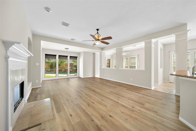 3106 Rainbow Ct, Pearland, TX 77584 - unfurnished living room featuring a ceiling fan, light wood finished floors, a fireplace, and decorative columns