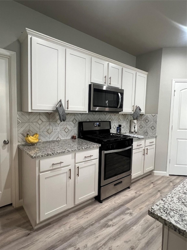 11577 Gingerland Dr, Conroe, TX 77304 - kitchen with appliances with stainless steel finishes, white cabinetry, tasteful backsplash, light wood-style flooring, and light stone counters