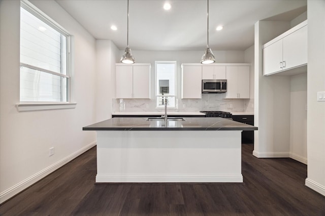 1805 Mills St, Houston, TX 77026 - kitchen featuring stainless steel microwave, a center island with sink, tasteful backsplash, white cabinetry, and dark wood-type flooring
