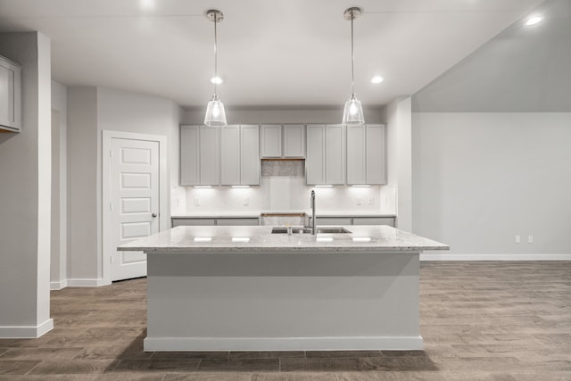 15215 Statice Trl, Houston, TX 77044 - kitchen with wood finished floors, a kitchen island with sink, light stone counters, pendant lighting, and backsplash