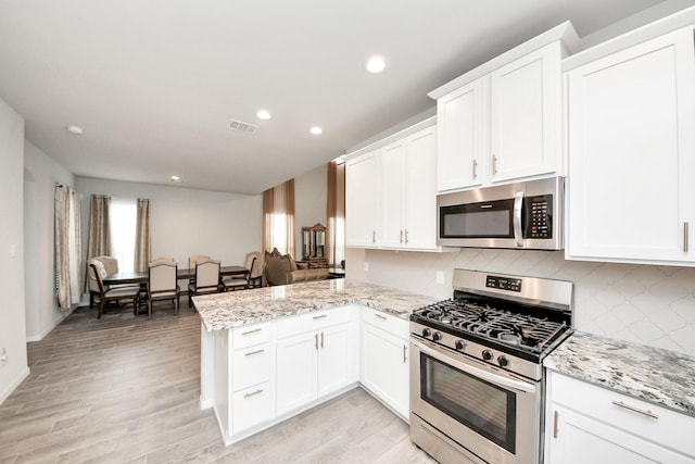 12306 Belhaven Terrace Dr, Houston, TX 77044 - kitchen featuring appliances with stainless steel finishes, a peninsula, backsplash, white cabinetry, and recessed lighting