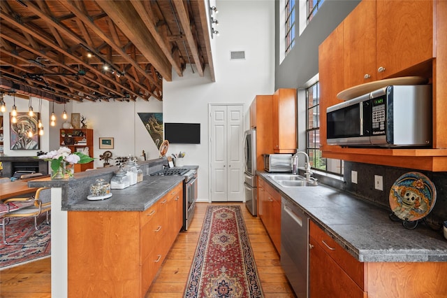 2614 Yoakum Blvd, Houston, TX 77006 - kitchen with appliances with stainless steel finishes, brown cabinetry, light wood finished floors, and a towering ceiling