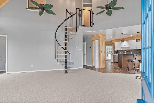 12901 E Barcelona, Galveston, TX 77554 - entryway with dark colored carpet, a towering ceiling, a ceiling fan, stairs, and wood walls