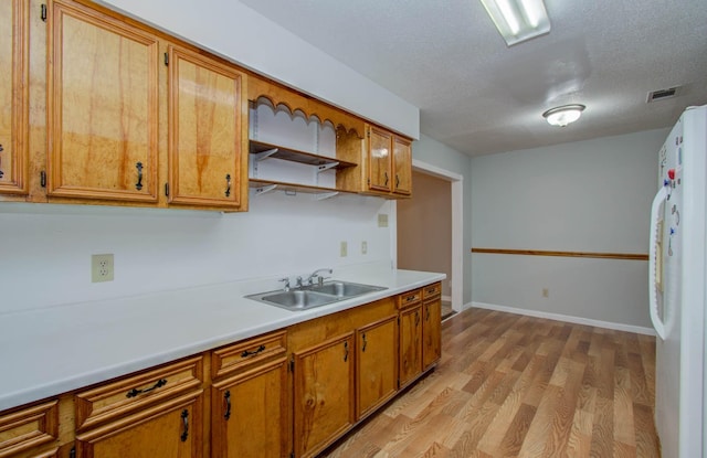 10131 Tangiers Rd, Houston, TX 77041 - kitchen with freestanding refrigerator, light wood-style flooring, brown cabinets, light countertops, and a textured ceiling