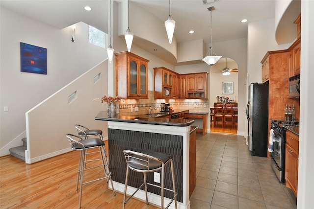 826 E 29th St, Houston, TX 77009 - kitchen featuring stainless steel appliances, brown cabinets, tasteful backsplash, a peninsula, and glass insert cabinets