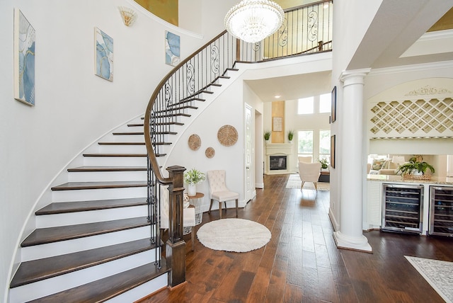 5450 Pudman River Ln, Sugar Land, TX 77479 - staircase featuring beverage cooler, decorative columns, a towering ceiling, hardwood / wood-style flooring, and a glass covered fireplace