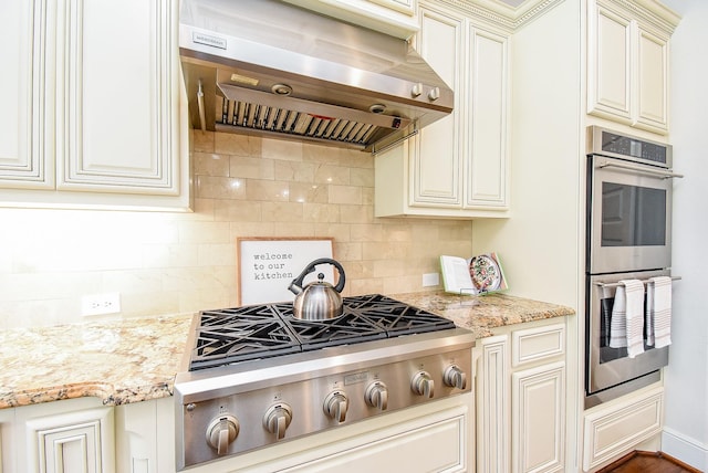 5450 Pudman River Ln, Sugar Land, TX 77479 - kitchen with wall chimney range hood, appliances with stainless steel finishes, backsplash, light stone counters, and cream cabinets