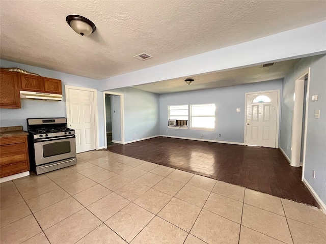 3707 Rosemont St, Houston, TX 77051 - kitchen with stainless steel gas range, under cabinet range hood, brown cabinetry, light tile patterned floors, and a textured ceiling