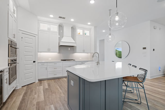 18615 Parkland Xing, Cypress, TX 77433 - kitchen with custom exhaust hood, gas stovetop, light wood-style flooring, light countertops, and a kitchen breakfast bar