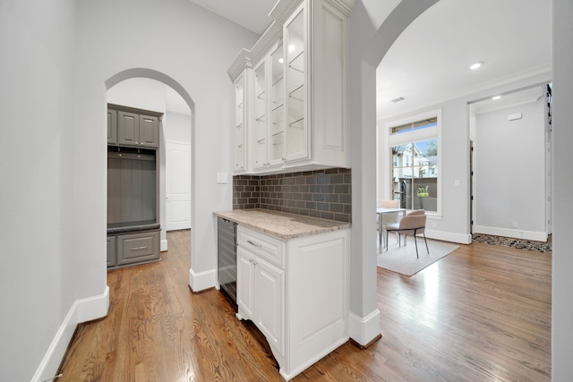 1302 Westview Garden Ct, Houston, TX 77055 - kitchen with arched walkways, wood finished floors, tasteful backsplash, glass insert cabinets, and white cabinetry