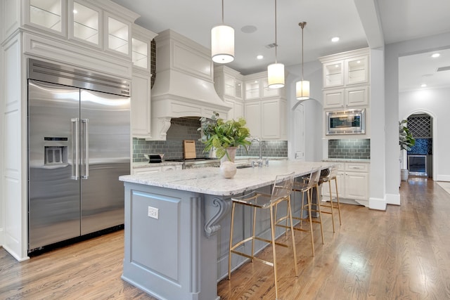 1302 Westview Garden Ct, Houston, TX 77055 - kitchen featuring built in appliances, light wood finished floors, backsplash, light stone counters, and white cabinets