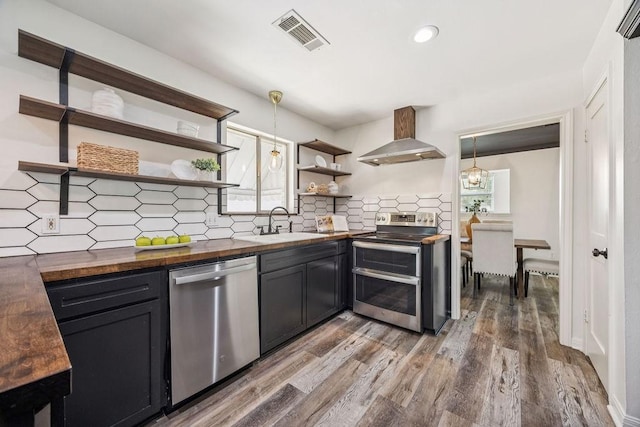 5515 Dumfries Dr, Houston, TX 77096 - kitchen with stainless steel appliances, butcher block countertops, open shelves, wall chimney range hood, and wood finished floors