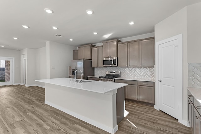 21521 Witham Promenade Ln, Magnolia, TX 77355 - kitchen featuring stainless steel appliances, an island with sink, tasteful backsplash, wood finished floors, and light countertops