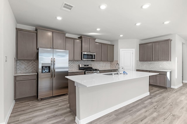 21521 Witham Promenade Ln, Magnolia, TX 77355 - kitchen featuring stainless steel appliances, backsplash, light wood-style floors, a kitchen island with sink, and recessed lighting