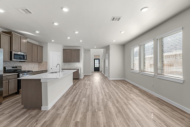 21521 Witham Promenade Ln, Magnolia, TX 77355 - kitchen featuring appliances with stainless steel finishes, tasteful backsplash, an island with sink, light wood-type flooring, and recessed lighting