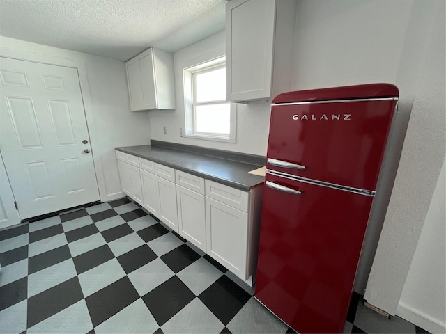 6625 Morris, Galveston, TX 77551 - kitchen featuring refrigerator, dark flooring, dark countertops, a textured ceiling, and white cabinetry