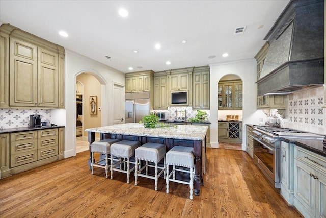 7614 Brykerwoods Dr, Houston, TX 77055 - kitchen with high end appliances, arched walkways, custom exhaust hood, a kitchen breakfast bar, and decorative backsplash