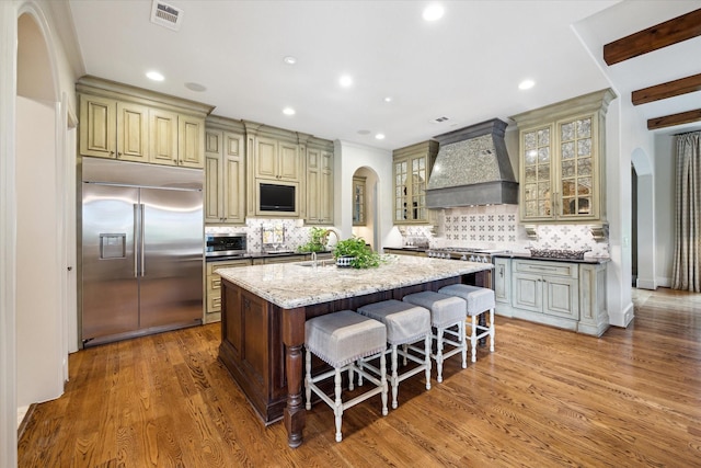 7614 Brykerwoods Dr, Houston, TX 77055 - kitchen with premium appliances, premium range hood, arched walkways, an island with sink, and cream cabinetry
