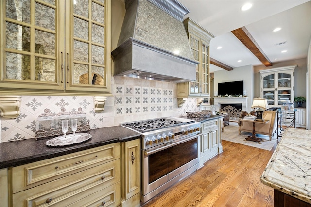 7614 Brykerwoods Dr, Houston, TX 77055 - kitchen featuring range with two ovens, custom exhaust hood, light wood finished floors, cream cabinets, and beamed ceiling