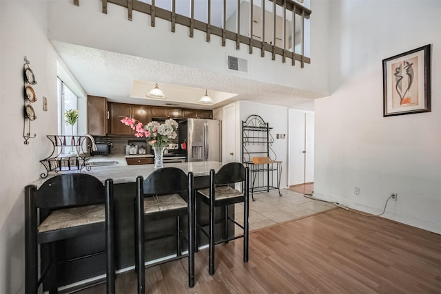 7642 Candlegreen Ln, Houston, TX 77071 - kitchen featuring stainless steel refrigerator with ice dispenser, a peninsula, light wood-style floors, a tray ceiling, and light countertops