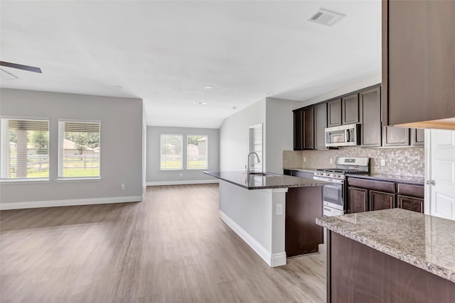214 Kickapoo Dr, Anahuac, TX 77514 - kitchen with appliances with stainless steel finishes, open floor plan, light wood-style flooring, decorative backsplash, and an island with sink