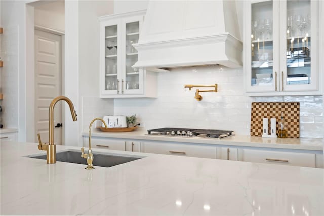 11822 Creekside Shore Cir, Cypress, TX 77433 - kitchen with custom range hood, stainless steel gas stovetop, white cabinets, and decorative backsplash