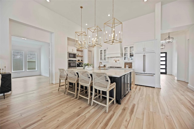 11822 Creekside Shore Cir, Cypress, TX 77433 - kitchen featuring built in appliances, light countertops, custom exhaust hood, a towering ceiling, and white cabinetry