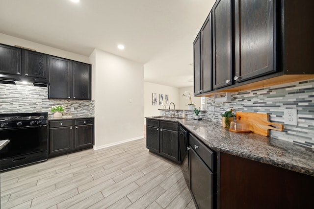 14722 Ruddy Duck Ln, Houston, TX 77049 - kitchen with black gas range oven, under cabinet range hood, tasteful backsplash, dark stone countertops, and light wood-type flooring