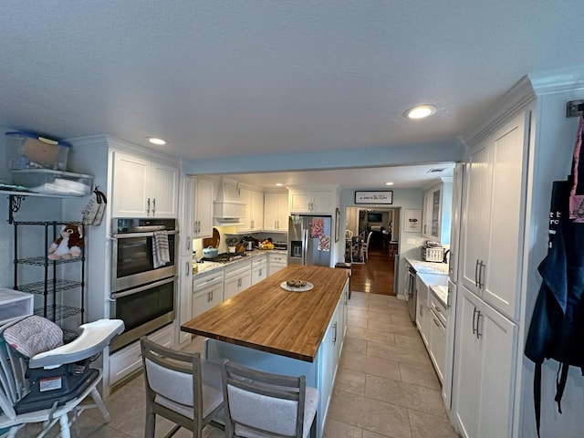 2201 Oleander Dr, Dickinson, TX 77539 - kitchen with butcher block counters, stainless steel appliances, white cabinets, a center island, and recessed lighting
