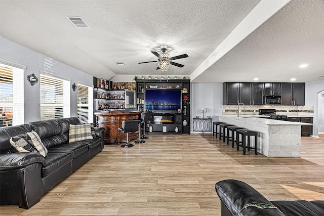 15307 Meandering Post Trl, Houston, TX 77044 - living room with a ceiling fan, a textured ceiling, light wood-style floors, and a dry bar