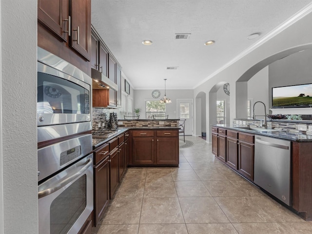 3310 Compass Ct, Conroe, TX 77301 - kitchen featuring appliances with stainless steel finishes, a peninsula, under cabinet range hood, ornamental molding, and backsplash