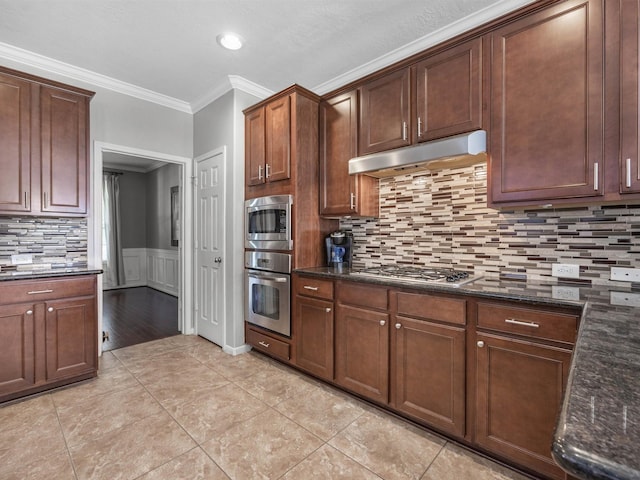 3310 Compass Ct, Conroe, TX 77301 - kitchen with stainless steel appliances, under cabinet range hood, ornamental molding, dark stone counters, and a wainscoted wall