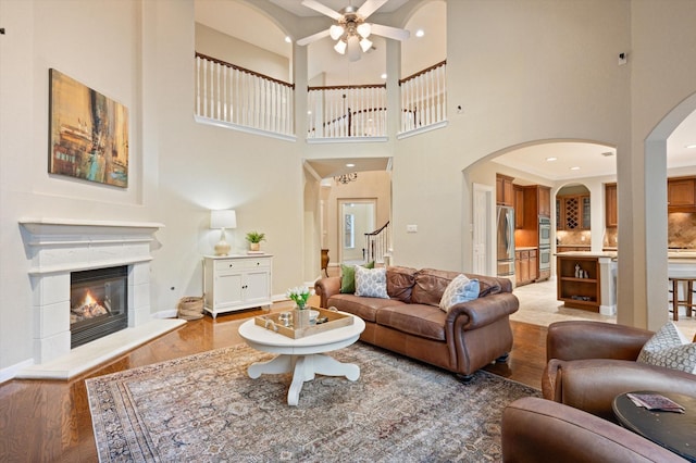 5222 Arcadia Glen Ln, Katy, TX 77494 - living room featuring light wood-style flooring, ceiling fan, a glass covered fireplace, a towering ceiling, and arched walkways