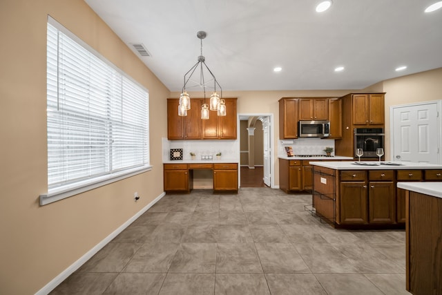 31322 Capella Cir, Tomball, TX 77375 - kitchen with stainless steel microwave, brown cabinets, light countertops, hanging light fixtures, and backsplash