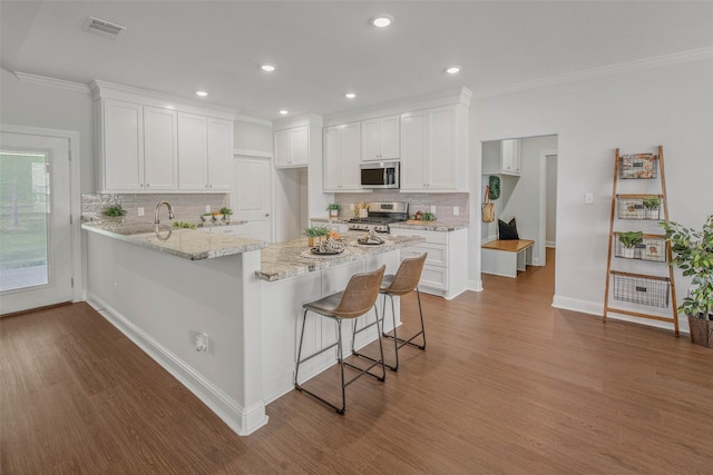9868 Albert Dr, Iola, TX 77861 - kitchen with appliances with stainless steel finishes, a peninsula, wood finished floors, white cabinets, and ornamental molding