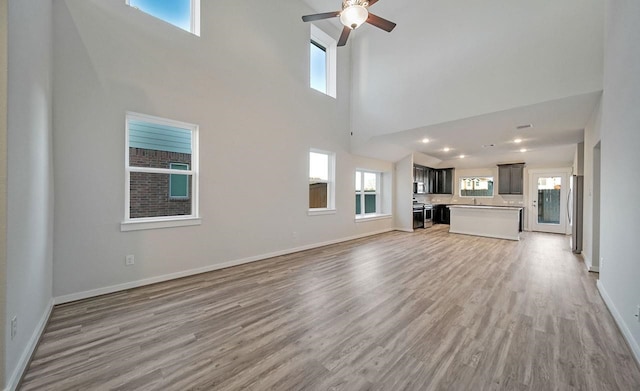 4446 Azalea Blossom Rd, Pinehurst, TX 77362 - unfurnished living room featuring light wood-style flooring, a ceiling fan, healthy amount of natural light, and a towering ceiling