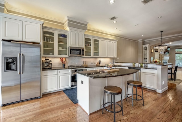 1013 Crocker St, Houston, TX 77019 - kitchen featuring stainless steel appliances, a peninsula, crown molding, light wood-style floors, and glass insert cabinets