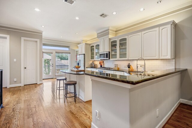 1013 Crocker St, Houston, TX 77019 - kitchen with stainless steel appliances, a breakfast bar area, crown molding, glass insert cabinets, and light wood-style floors