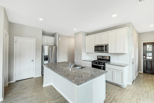 25707 Boxwood Hedge Ln, Tomball, TX 77375 - kitchen with appliances with stainless steel finishes, light wood-style flooring, an island with sink, backsplash, and light stone counters
