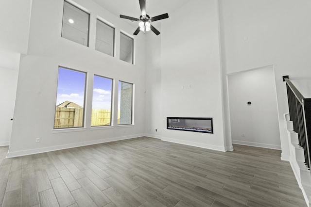 5021 Steady Breeze Dr, Katy, TX 77493 - unfurnished living room featuring a high ceiling, ceiling fan, wood finished floors, a glass covered fireplace, and stairway