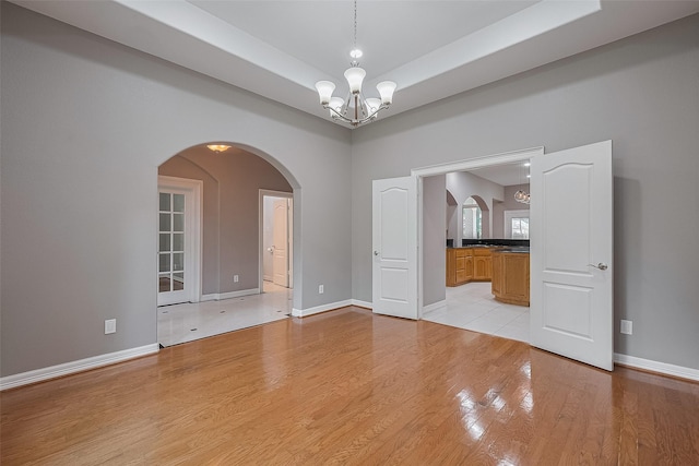 6210 Mahogany Way, Magnolia, TX 77354 - empty room with a chandelier, arched walkways, light wood-style floors, and a tray ceiling